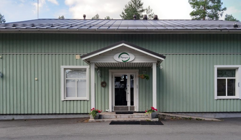 Sisäänkäynti vihreään puutaloon. Vasemmalla puolella ja oikealla puolella sisäänkäyntiä on ikkunat.Keskellä sisäänkäyntiä lukee Peiponpesä. Sisäänkäynnin molemmin puolin on pinkit kukat kukkaruukuissa.