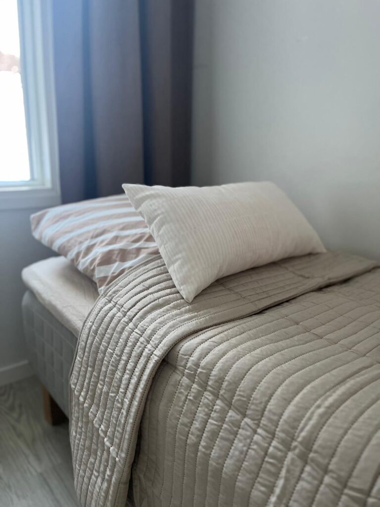 Familar Ylöjärvi: yhden hengen sänky jolle on levitetty siisti päiväpeitto, taustalla olevasta ikkunasta paistaa valoa sisään