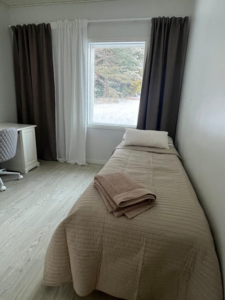 Huoneen sisustusta Familar Ylöjärvellä. Yhden hengen sänky, verhot ikkunoissa, pieni työpöytä ja tuoli