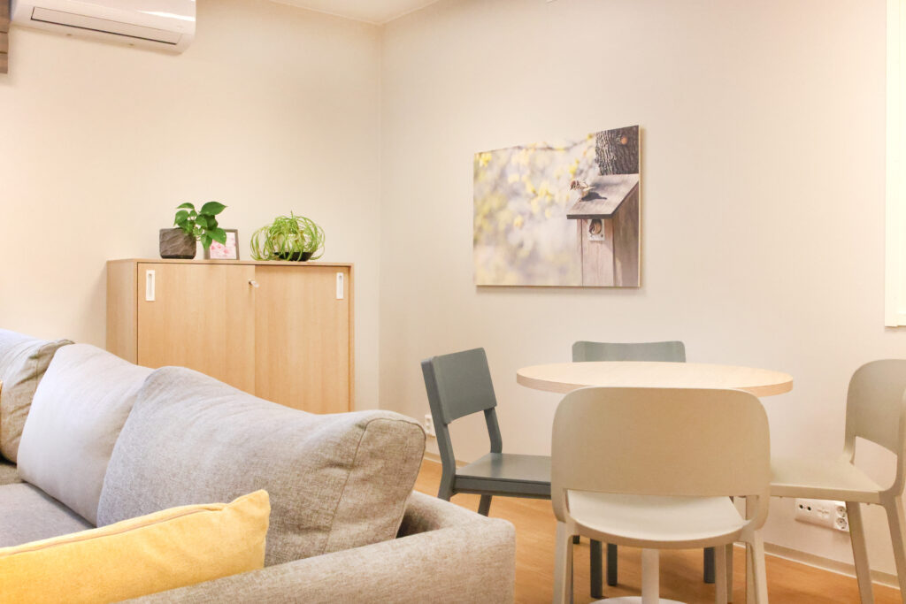 Huone, jossa pyöreä pöytä, puunvärinen lipasto, jonka päällä kasveja. Seinällä taulu.