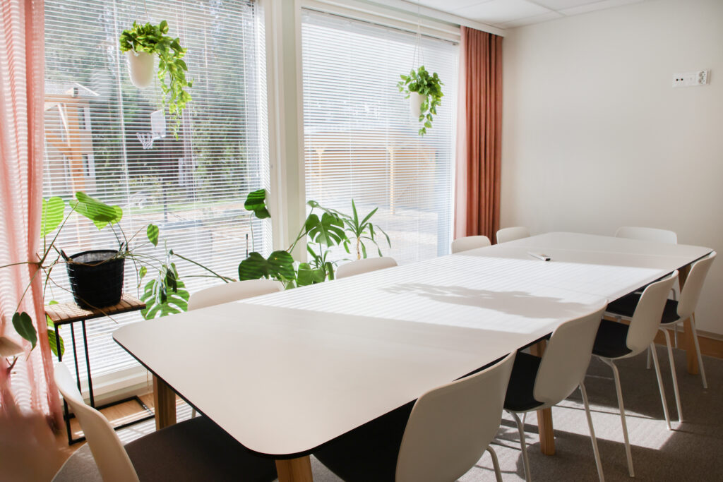 Valkoinen pitkä pöytä huoneessa, jossa isot ikkunat ja kasveja.