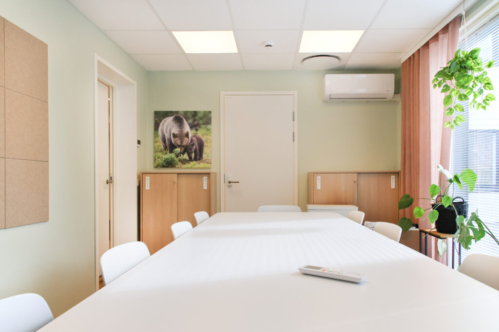 Yksikkö sisältä, pitkä valkoinen pöytä ja ruskeat lipastot, viherkasveja.