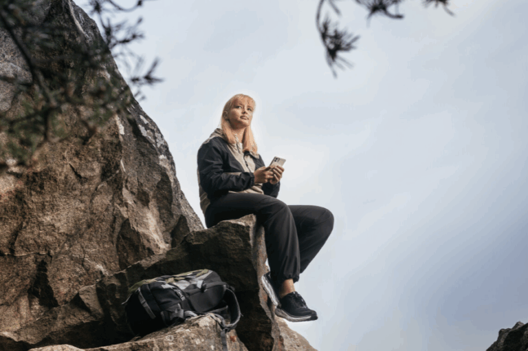 Nuori istuu kalliolla puhelin kädessä